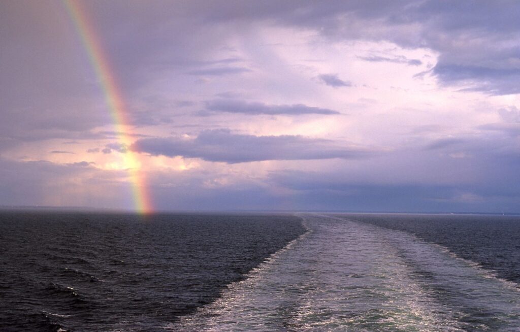 A rainbow over the ocean and a boat in the water.