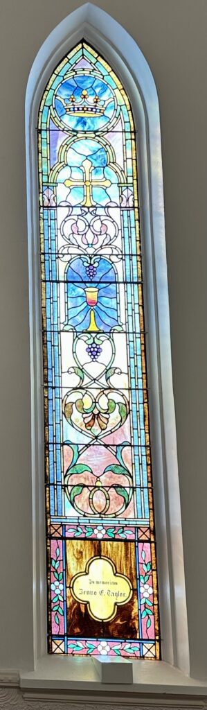 A stained glass window with grapes and a vase.