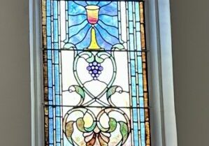 A stained glass window with grapes and a vase.