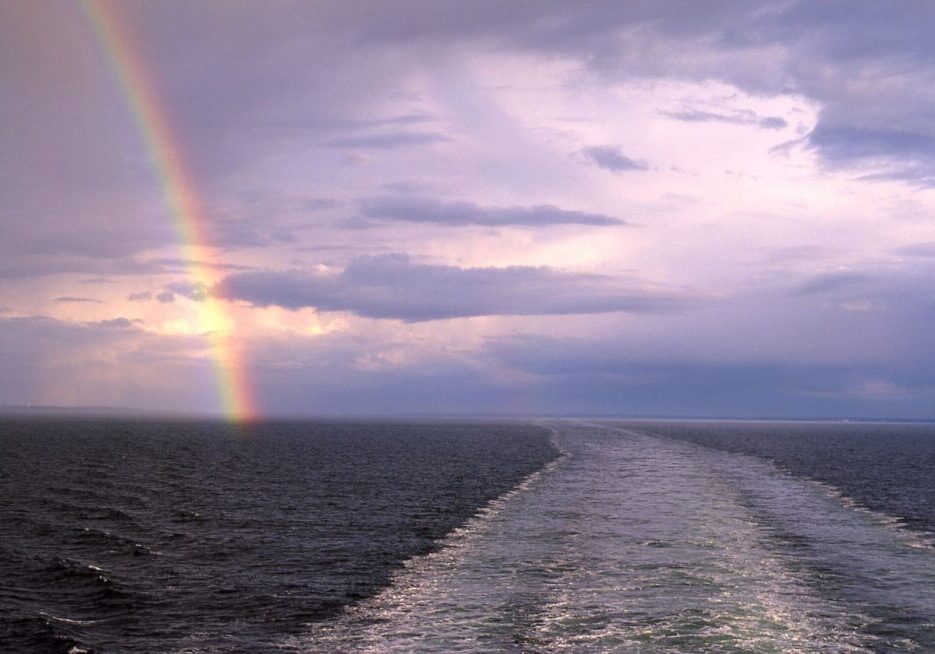 A rainbow over the ocean and a boat in the water.