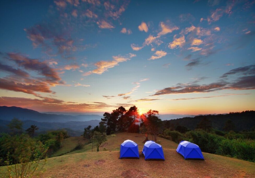 Three blue tents on a hill with the sun setting.
